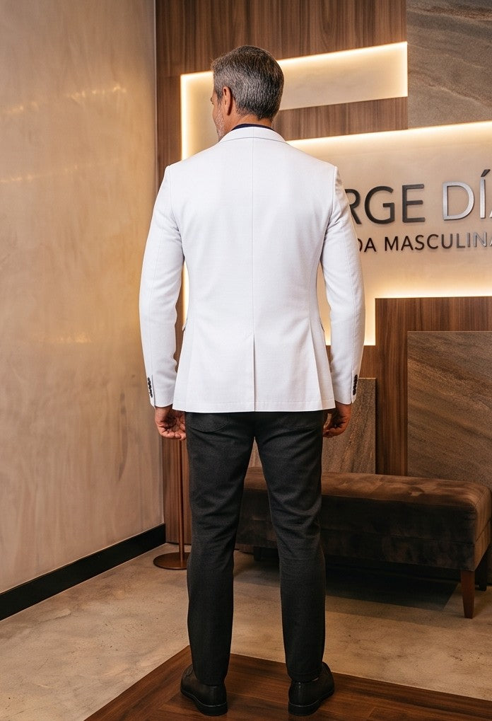 blazer blanco roto para hombre, confeccionado en un tejido con textura táctil tipo lino. La prenda presenta solapas de muesca, un cierre de dos botones, bolsillos de parche y costuras decorativas visibles que resaltan un diseño artesanal y sofisticado, ideal para un estilo casual-elegante