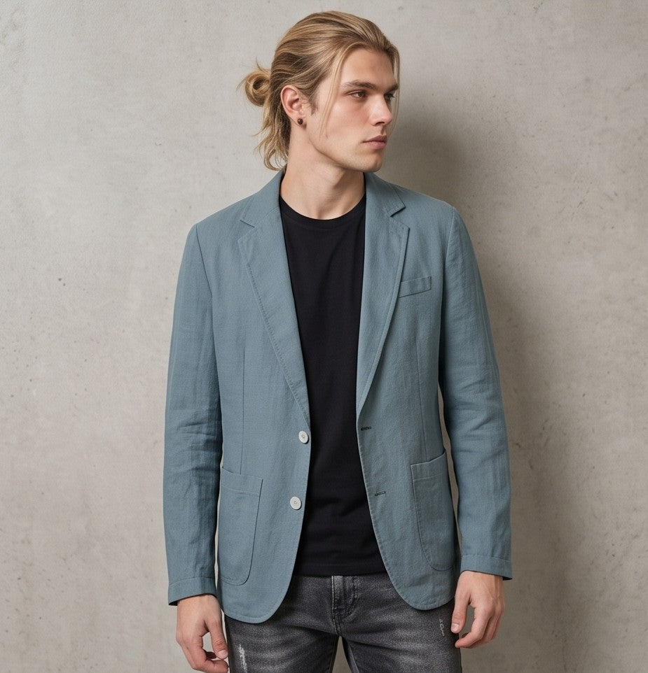 blazer de lino desestructurado para hombre. La prenda, de corte casual y ligero, muestra la textura granulada natural del lino. Tiene solapas de muesca, un cierre de dos botones frontales y dos grandes bolsillos de parche aplicados en la cintura.