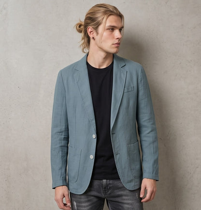 blazer de lino desestructurado para hombre. La prenda, de corte casual y ligero, muestra la textura granulada natural del lino. Tiene solapas de muesca, un cierre de dos botones frontales y dos grandes bolsillos de parche aplicados en la cintura.
