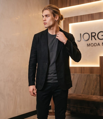 blazer de lino desestructurado para hombre. La prenda, de corte casual y ligero, muestra la textura granulada natural del lino. Tiene solapas de muesca, un cierre de dos botones frontales y dos grandes bolsillos de parche aplicados en la cintura.