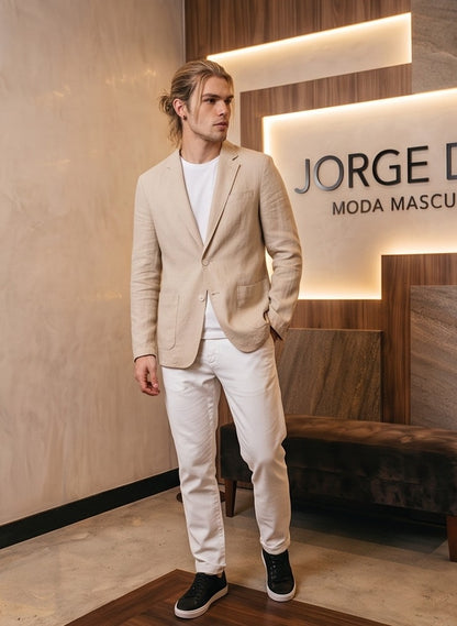 blazer de lino desestructurado para hombre. La prenda, de corte casual y ligero, muestra la textura granulada natural del lino. Tiene solapas de muesca, un cierre de dos botones frontales y dos grandes bolsillos de parche aplicados en la cintura.