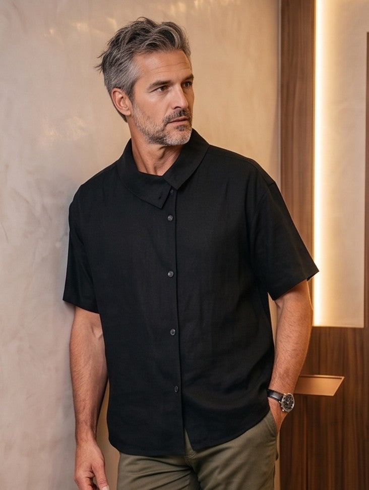 Camisa casual de manga corta holgada para hombre con textura ligera tipo lino, cuello asimétrico y botones frontales, disponible en color negro y beige arena sobre fondo neutro