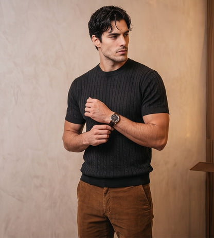 Hombre luciendo una camiseta de punto trenzado de manga corta y cuello redondo. Diseño de textura en relieve con ajuste entallado que resalta la figura masculina. Prenda de estilo smart-casual, disponible en colores neutros y versátiles (beige, blanco y negro), combinada con diferentes pantalones para un look moderno y elegante
