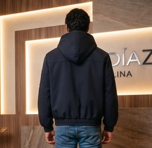 Chaqueta bomber para hombre con capucha, confeccionada en tejido liso disponible en color negro y azul marino, con bolsillos delanteros, bolsillo utilitario con cremallera plateada en la manga, bajo elástico fruncido y cierres metálicos tipo mosquetón al frente