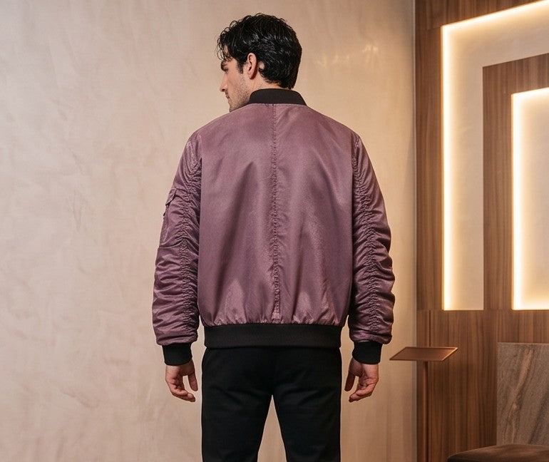 Chaqueta bomber de corte holgado para hombre en tono monocolor con acabado lavado disponible en morado ciruela y gris grafito oscuro. Destaca por mangas largas fruncidas tipo stacked, bolsillo utilitario con cremallera en el brazo, cierre central de cremallera con broches metálicos delanteros y cuello y puños elásticos acanalados en negro
