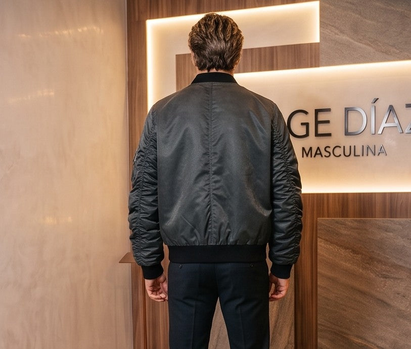 Chaqueta bomber de corte holgado para hombre en tono monocolor con acabado lavado disponible en morado ciruela y gris grafito oscuro. Destaca por mangas largas fruncidas tipo stacked, bolsillo utilitario con cremallera en el brazo, cierre central de cremallera con broches metálicos delanteros y cuello y puños elásticos acanalados en negro