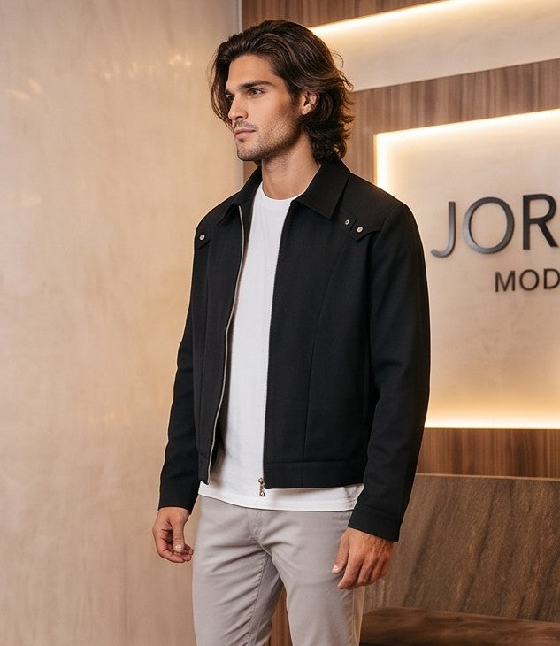 Chaqueta entallada slim fit para hombre disponible en color negro y azul marino, confeccionada en tejido liso estructurado con cuello camisero, cremallera metálica frontal central, puños con cierre a presión y detalles decorativos de solapa en los hombros sobre fondo de estudio minimalista