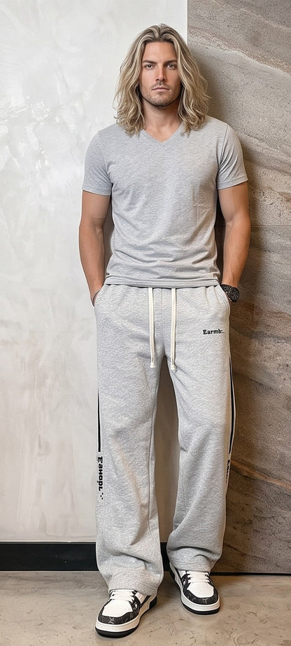 Pantalón jogger deportivo y casual para hombre de corte ancho y tiro medio, con cintura elástica con cordón ajustable, franjas laterales a contraste con detalle de texto estampado y bolsillos funcionales, disponible en color negro y gris jaspeado