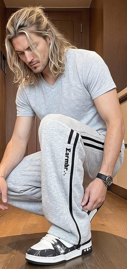 Pantalón jogger deportivo y casual para hombre de corte ancho y tiro medio, con cintura elástica con cordón ajustable, franjas laterales a contraste con detalle de texto estampado y bolsillos funcionales, disponible en color negro y gris jaspeado