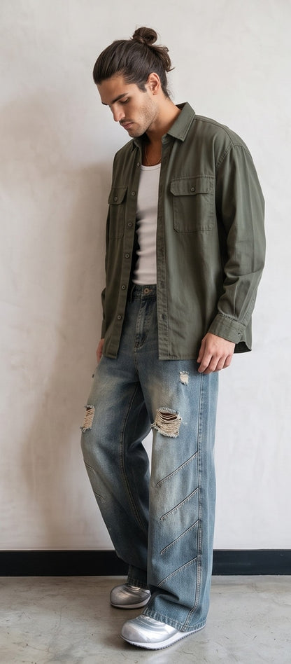 Pantalón jean ancho estilo urbano streetwear en denim 100% algodón con efecto lavado en tonos azul y negro desgastado, tiro medio-alto, cintura semielástica con botón y cremallera, roturas desgastadas en rodillas y bordados diagonales decorativos en las piernas