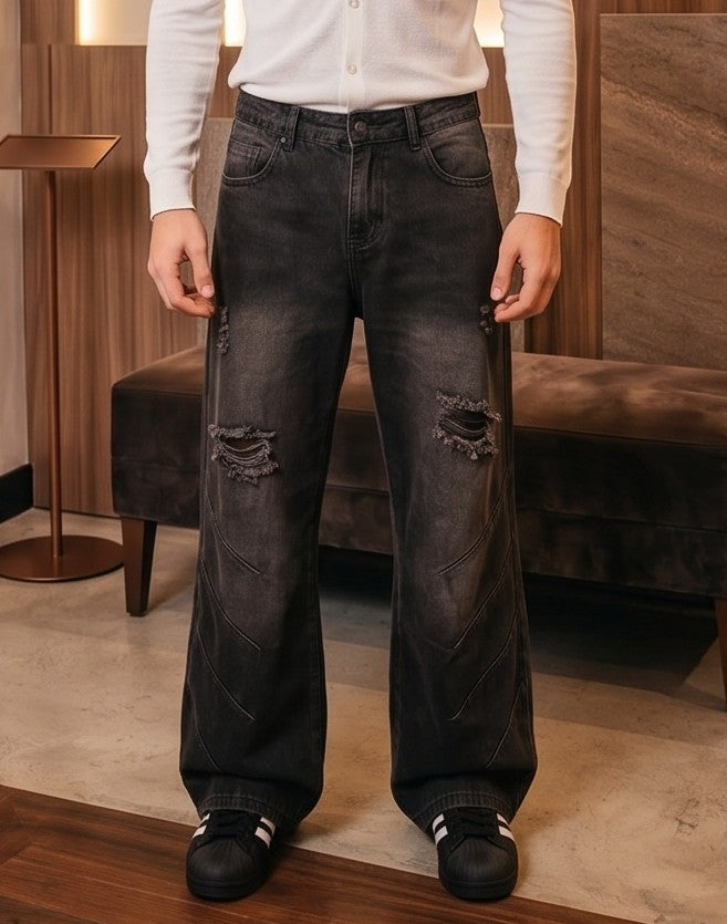 Pantalón jean ancho estilo urbano streetwear en denim 100% algodón con efecto lavado en tonos azul y negro desgastado, tiro medio-alto, cintura semielástica con botón y cremallera, roturas desgastadas en rodillas y bordados diagonales decorativos en las piernas