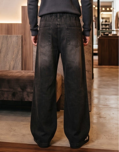 Pantalón jean ancho estilo urbano streetwear en denim 100% algodón con efecto lavado en tonos azul y negro desgastado, tiro medio-alto, cintura semielástica con botón y cremallera, roturas desgastadas en rodillas y bordados diagonales decorativos en las piernas
