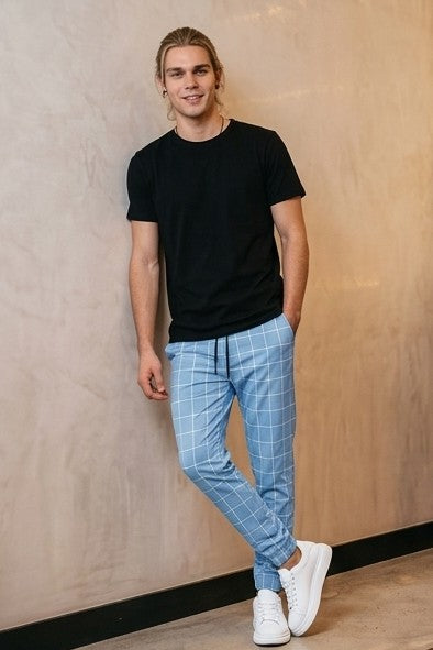 Pantalones estilo jogger para hombre con un elegante patrón de cuadros tipo ventana (windowpane grid). La prenda cuenta con una cintura elástica ajustable mediante cordón, bolsillos laterales prácticos y un ajuste ceñido pero cómodo que se estrecha hacia los tobillos. Está disponible en una gama de colores que incluye azul claro, beige, azul marino, gris oscuro y negro, todos con las líneas de los cuadros en contraste blanco.