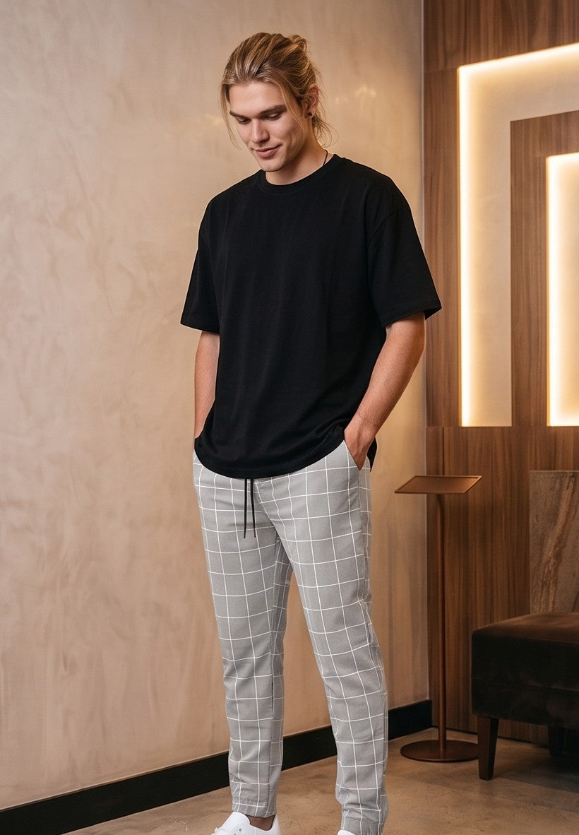 Pantalones estilo jogger para hombre con un elegante patrón de cuadros tipo ventana (windowpane grid). La prenda cuenta con una cintura elástica ajustable mediante cordón, bolsillos laterales prácticos y un ajuste ceñido pero cómodo que se estrecha hacia los tobillos. Está disponible en una gama de colores que incluye azul claro, beige, azul marino, gris oscuro y negro, todos con las líneas de los cuadros en contraste blanco.