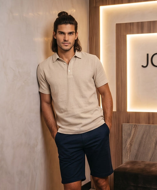 polo de hombre de manga corta, confeccionado en un tejido de lino de textura visible y transpirable. La prenda presenta un cuello clásico estructurado y una tapeta frontal con botones pulidos. El corte es moderno y relajado, y está disponible en siete colores diferentes: beige natural, blanco, negro, azul marino, azul cielo, gris y verde oliva